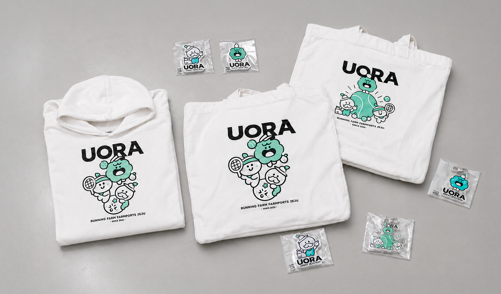 마플 단체 굿즈 – UORA 캐릭터 그래픽을 인쇄한 화이트 후드티와 에코백, 아크릴 키링으로 구성한 브랜드 굿즈 세트 이미지