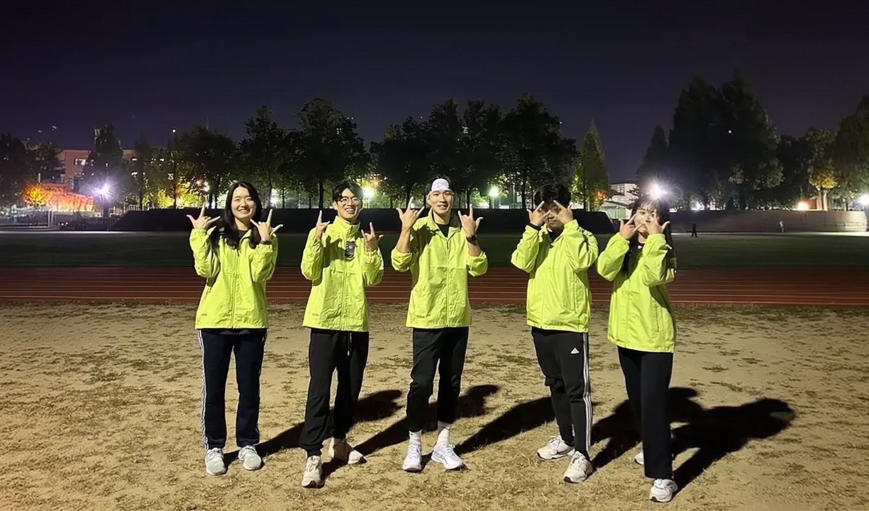 마플 바람막이 제작 - 가슴에 어두운 색 로고를 넣은 형광 연두색 바람막이를 맞춰 입고 야간 운동장에서 찍은 스포츠 크루 단체 사진