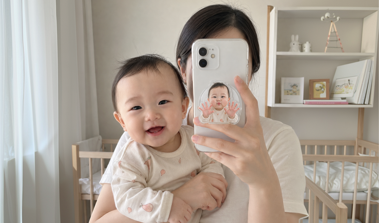 마플 아기 아크릴 스마트톡 – 아기 사진으로 만든 투명 커스텀 스마트톡을 스마트폰에 부착하고 아기를 안은 채 거울 셀카를 찍는 이미지