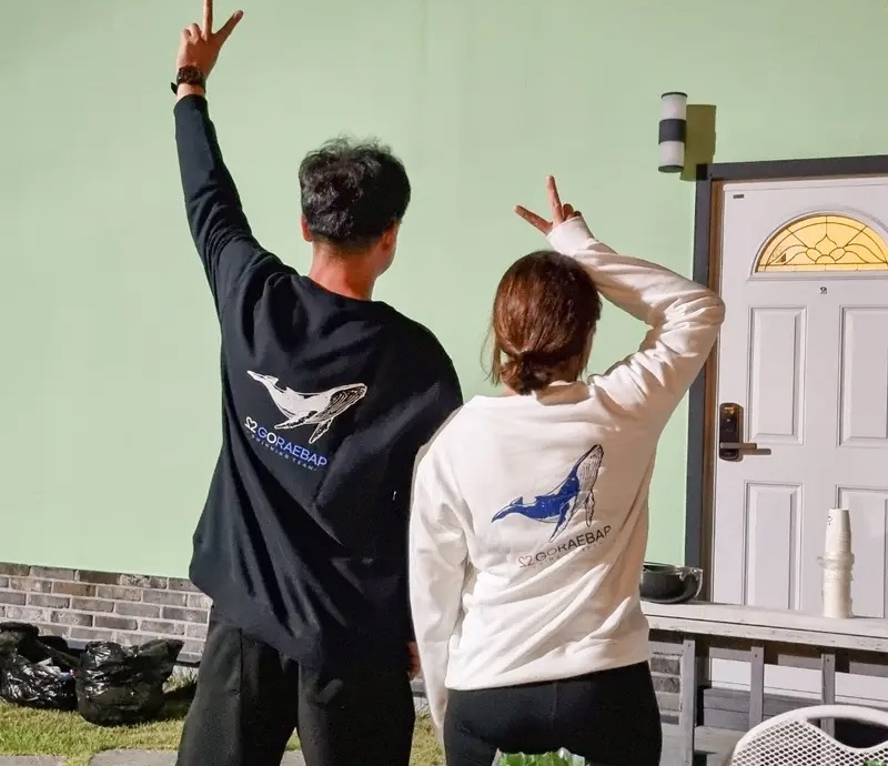 마플 커플 맨투맨 제작 – 고래 일러스트와 레터링을 등판에 프린팅한 블랙과 화이트 맨투맨을 맞춰 입은 두 사람의 뒷모습 이미지